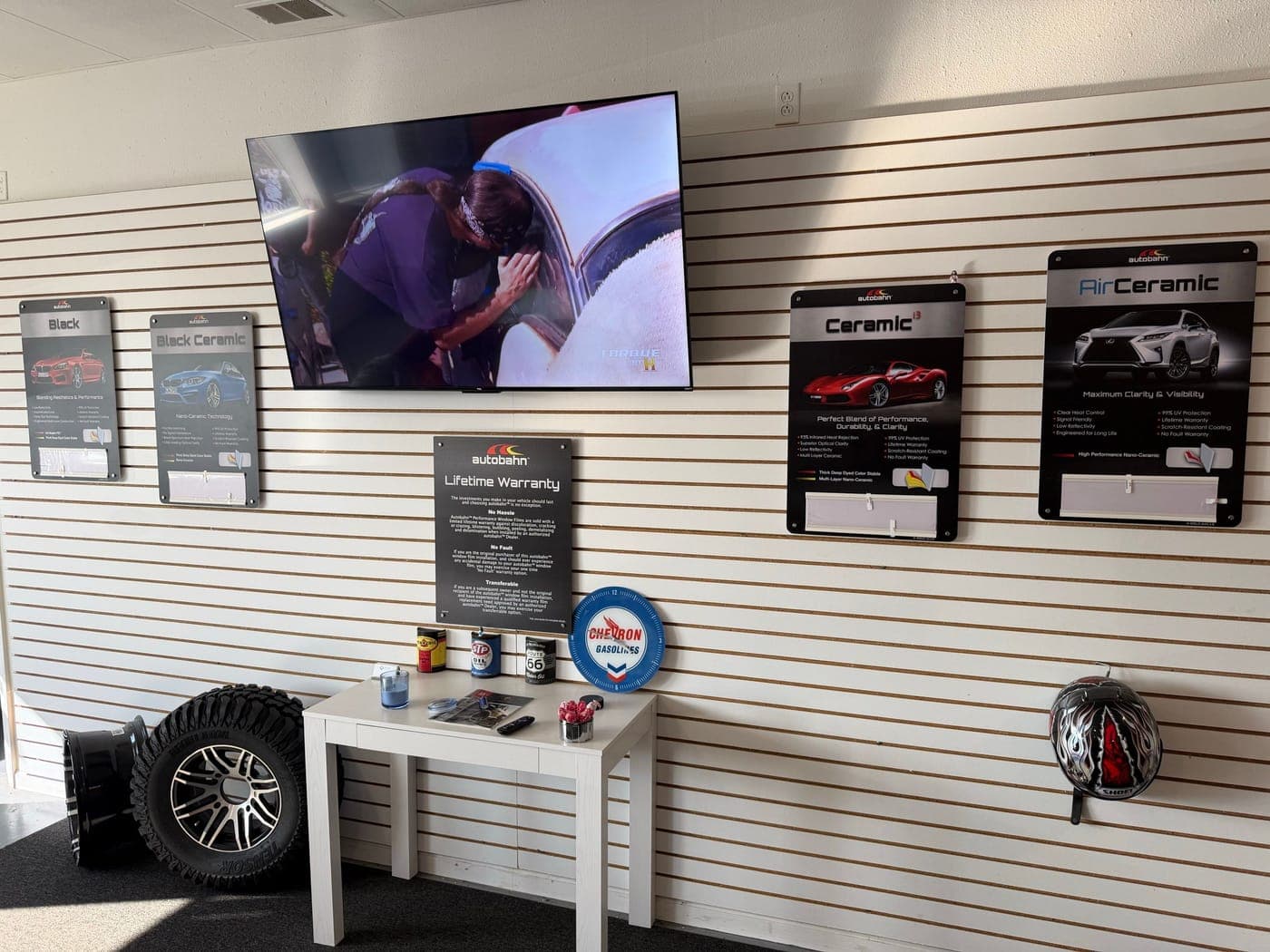 Customer area with window film and ceramic coating sample boards on a slat wall, a television, and a small table