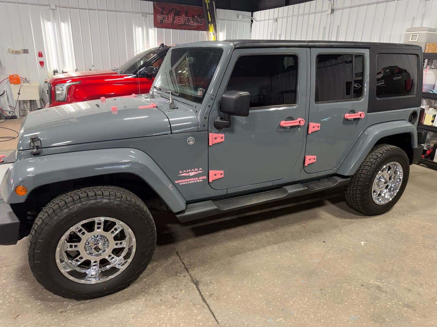 Gray Jeep Wrangler with pink door hinges parked in the indoor work bay