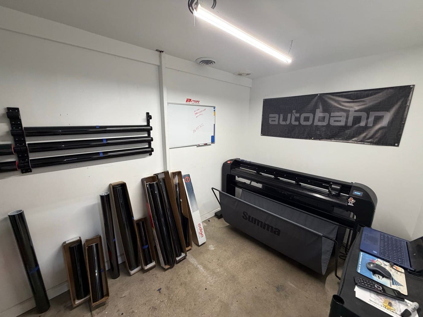 Tint plotter room with a Summa film cutter, stacked window-film rolls, and an Autobahn banner