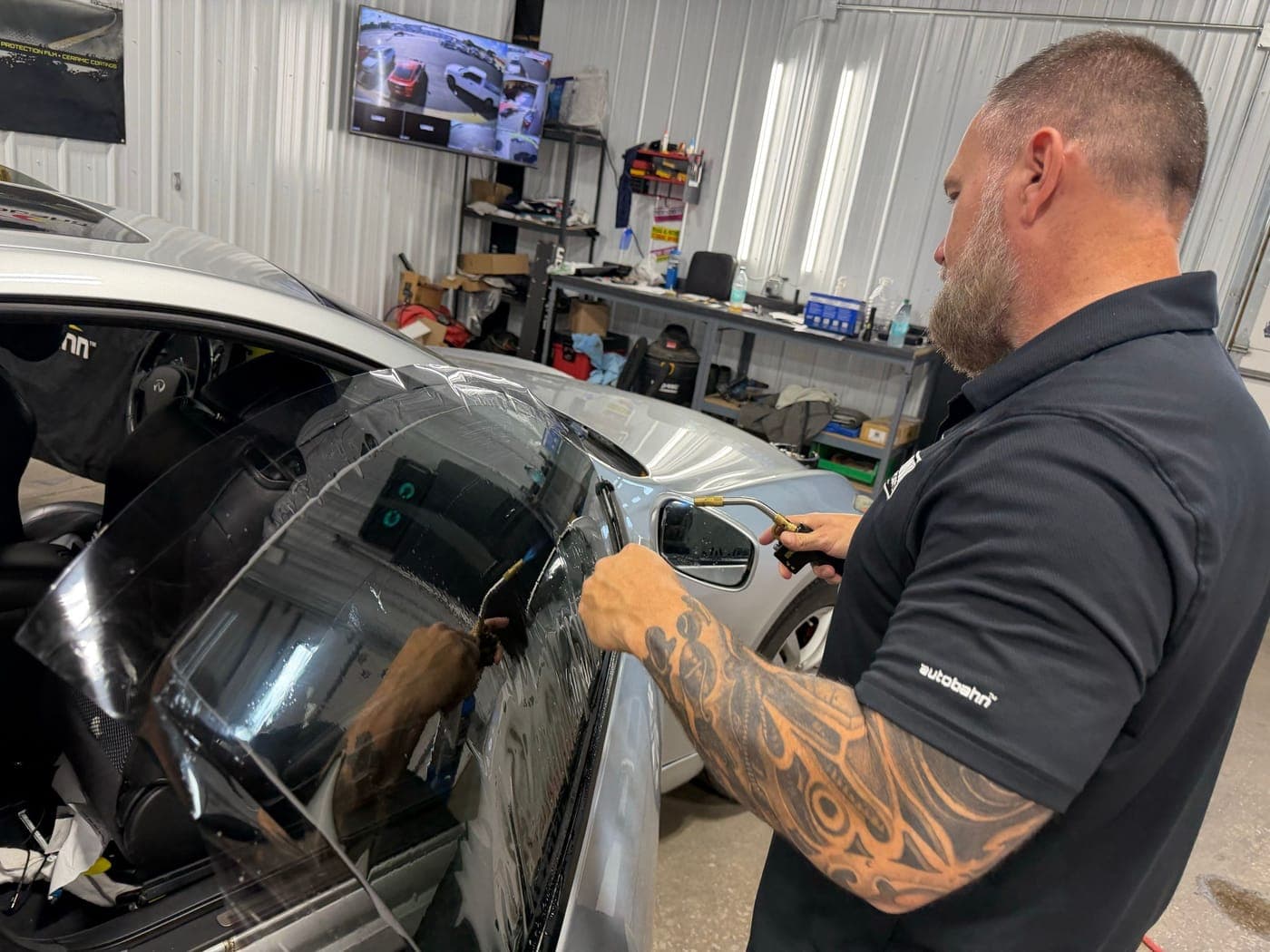 Tint technician applying window film to a silver car in the shop
