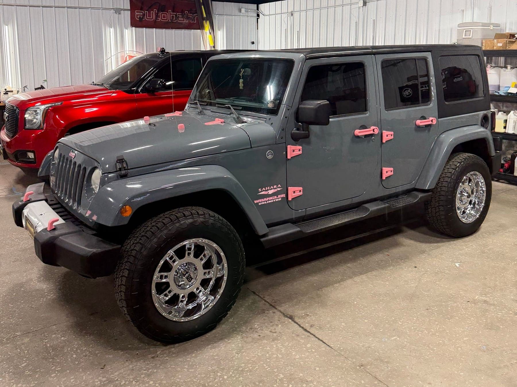 Gray Jeep Wrangler with pink accents beside a red SUV inside the Ironwood Motorsports shop